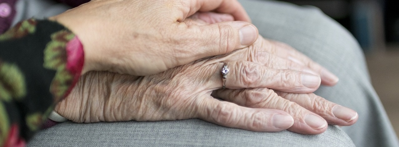 Dłoń obejmująca dłonie starszej kobiety.